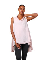 A woman wearing a pink sleeveless cowl neck top with an asymmetrical hem, paired with white trousers.