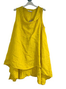 A woman wearing a yellow sleeveless cowl neck top with an asymmetrical hem, paired with white trousers.